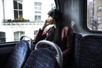 Молода жінка сидить у автобусі, носить навушники, дивиться з вікна — стокове фото