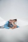 Boy lying on side between white bed sheets — Stock Photo