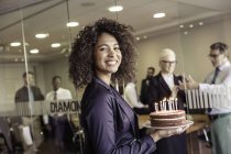 Jovem apresentando bolo com velas para equipe de negócios na sala de reuniões — Fotografia de Stock