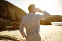 Mature man standing on beach, using smartphone, rear view, Cape Town, South Africa — Stock Photo