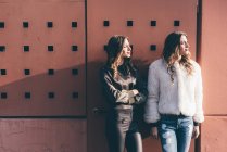 Portrait of twin sisters, outdoors, leaning against wall, looking away — Stock Photo