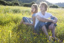Romantic young couple sitting back to back in wildflower field, Majorca, Spain — Stock Photo