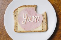 Vista superior de la palabra yum escrita en jamón y queso sobre pan en mayonesa - foto de stock