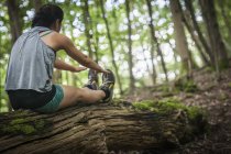 Woman exercising while sitting on log in forest — Stock Photo