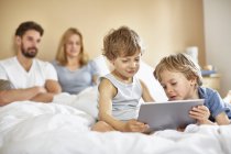 Garçons sur le lit des parents en utilisant une tablette numérique — Photo de stock