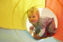 Retrato de uma menina rastejando em um túnel multicolorido — Fotografia de Stock