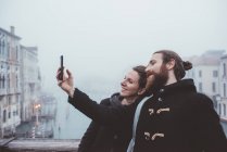 Couple taking smartphone selfie over misty canal, Venice, Italy — Stock Photo