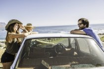 Tres amigos adultos medios apoyados en el techo del coche en la costa, Ciudad del Cabo, Sudáfrica - foto de stock