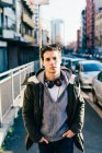 Man with headphones in urban area, hands in pockets looking at camera — Stock Photo