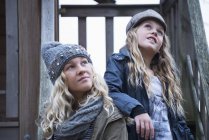 Blond haired sisters wearing knit and baker boy hats looking up from porch — Stock Photo
