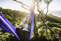 Female hiker looking at smartphone in hammock, Pacific Rim National Park, Vancouver Island, British Columbia, Canada — Stock Photo