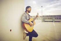 Mid adult man playing acoustic guitar on rooftop parking lot — Stock Photo