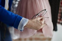 Vue recadrée de la femme tenant des lunettes de vue examinant robe en mousseline de soie — Photo de stock