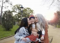 Mother and grandmother kissing smiling girls cheeks — Stock Photo