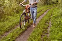 Cuello abajo vista del hombre empujando bicicleta en pista de tierra rural - foto de stock