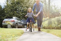 Батько навчає дочку їздити на велосипеді на вулиці — стокове фото