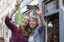 Жінки перед магазином тримають відкритий знак, приймаючи селфі зі смартфоном — стокове фото