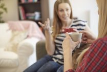 Two female friends, sitting on sofa, drinking coffee, catching up — Stock Photo