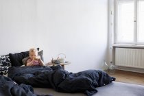 Menina, sentada na cama, bebendo de mamadeira — Fotografia de Stock