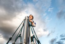 Junge im Astronautenkostüm starrt auf Klettergerüst vor dramatischem Himmel — Stockfoto