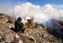 Hombre en el borde del cráter del volcán Gorely, mirando la pluma de gas y vapor, península de Kamchatka, Rusia - foto de stock