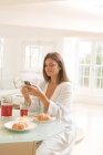 Reife Frau am Frühstückstisch liest Handytexte — Stockfoto