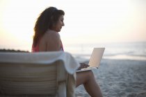 Mature woman sitting on beach sun lounger looking at laptop, Dubai, United Arab Emirates — Stock Photo