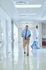 Médico sênior caminhando pelo corredor do hospital lendo anotações médicas — Fotografia de Stock