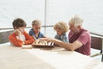 Abuelo y nietos jugando ajedrez - foto de stock