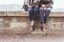 Waist down view of young couple sitting on harbour wall, Lake Como, Italy — Stock Photo