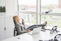Madura mujer de negocios con los pies en el escritorio de la oficina - foto de stock