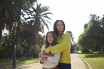 Мать, стоящая позади дочери в парке, смотрит в сторону — стоковое фото