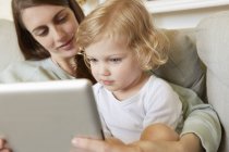 Female toddler sitting on mother's knee looking at digital tablet — Stock Photo