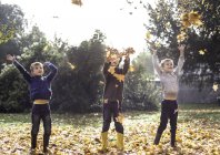 Tre ragazzi all'aperto, lanciando foglie autunnali — Foto stock