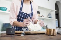 Обрезанный снимок молодой женщины, растягивающей тесто на кухонном столе — стоковое фото