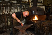 Caucasian male blacksmith at work in smith — Stock Photo