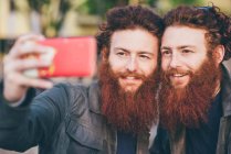 Jeune mâle hipster jumeaux avec des cheveux roux et barbe prendre smartphone selfie — Photo de stock