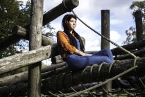 Mujer joven sentada en un marco de escalada de madera, con auriculares - foto de stock
