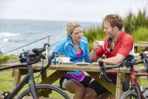 Велосипедисты отдыхают за столом для пикника с видом на океан — стоковое фото