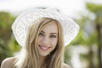 Portrait of beautiful blond young woman wearing straw hat in city — Stock Photo