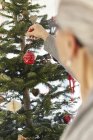 Seniorin stellt Christbaumkugel an Weihnachtsbaum — Stockfoto
