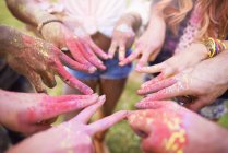 Група друзів на фестивалі, покрита барвистою порошковою фарбою, з'єднує пальці зі знаками миру, крупним планом — стокове фото
