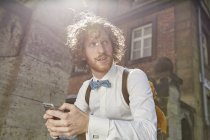 Young man outdoors, using smartphone, wearing shirt and bow tie — Stock Photo