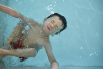 Niño con los ojos cerrados, con la cabeza sobre el agua en la piscina - foto de stock
