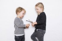 Young girl and boy leaning against white background, girl holding twigs — Stock Photo