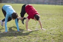 Junge Männer und Frauen machen Kniebeugen auf dem Spielfeld — Stockfoto