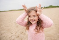 Bambina mostrando corna sulla testa in spiaggia — Foto stock