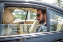 Молодой бизнесмен использует цифровой планшет на заднем сиденье автомобиля, Дубай, Объединенные Арабские Эмираты — стоковое фото