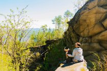 Femme randonneuse et son bouledogue assis sur un rocher de montagne regardant au-dessus de la forêt, Russie — Photo de stock