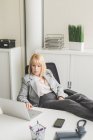 Reife Geschäftsfrau mit Füßen nach oben auf Büroschreibtisch mit Laptop — Stockfoto